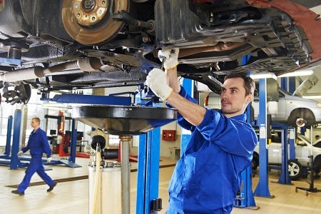 Mechanic working under a raised vehicle in a repair shop.
