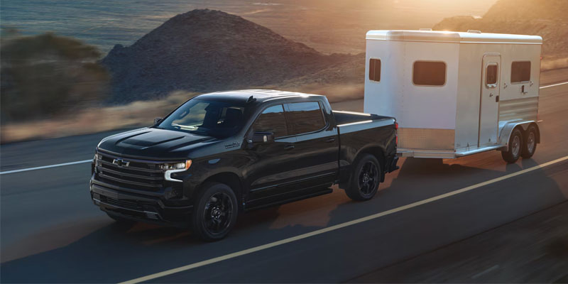 A black Chevy Silverado towing a white trailer on a road.
